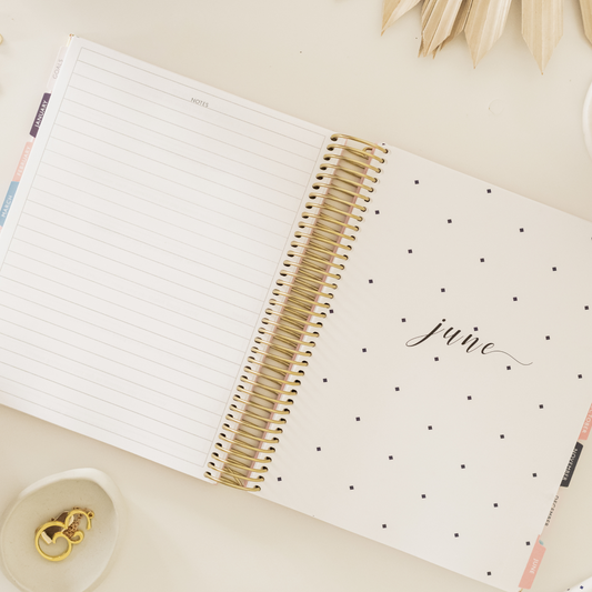 Planned and Proper planner open to a goal-setting page for women focused on productivity.  A 2025 weekly planner from Planned and Proper displayed with coffee and stationery.